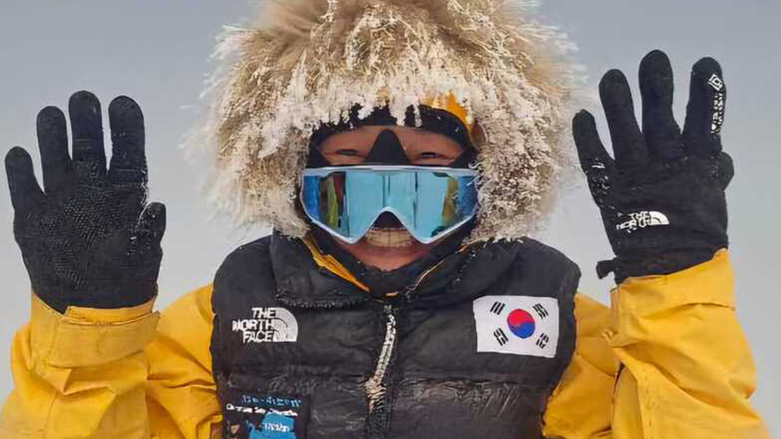 a woman in a fur-lined hood and visor holds up her hands