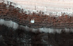 A block of white ice falls across dark red rock.