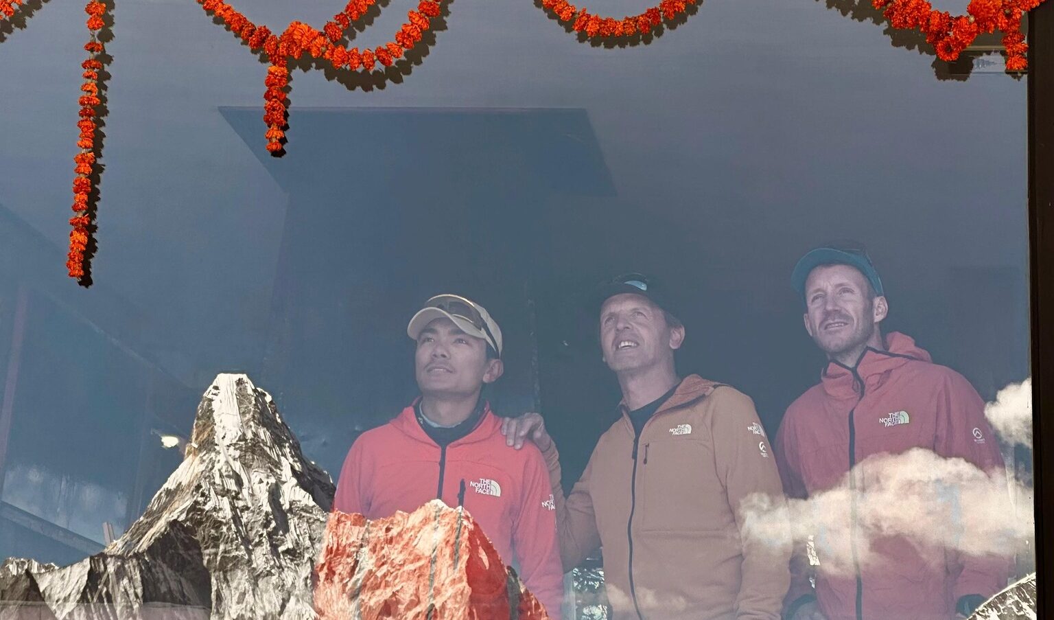 the climbers looking at Ama Dablam, relexed in the glass in front of them.