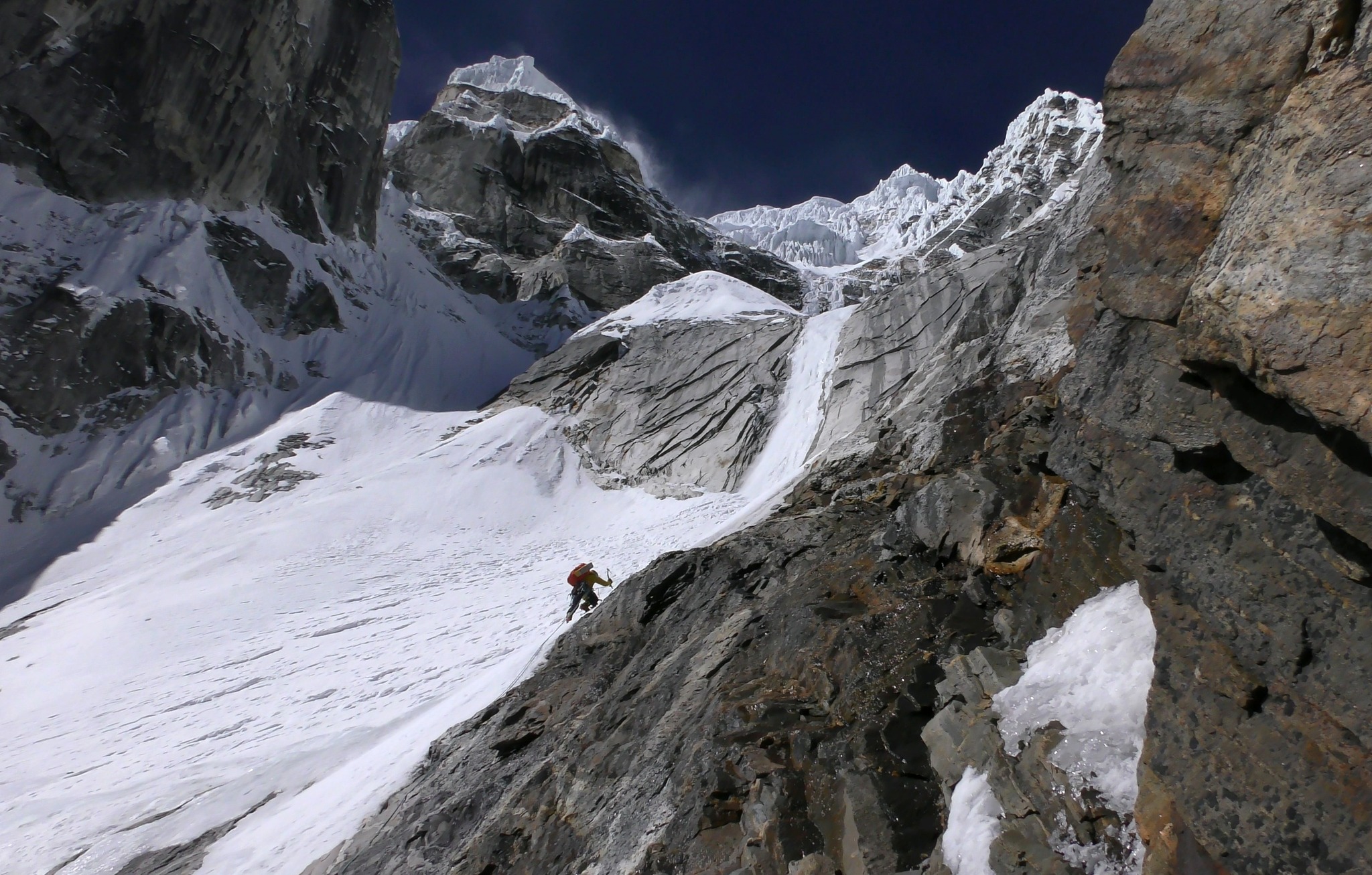 Gigantic face of rock and ice, with a frozen curtain of ice above a tiny climber.