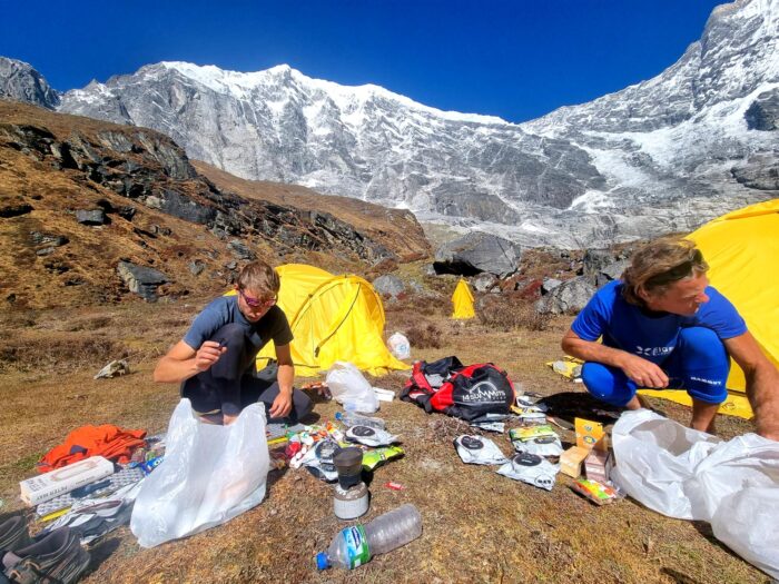 climbers sorting out gear in front of two yellow tents on grassy ground