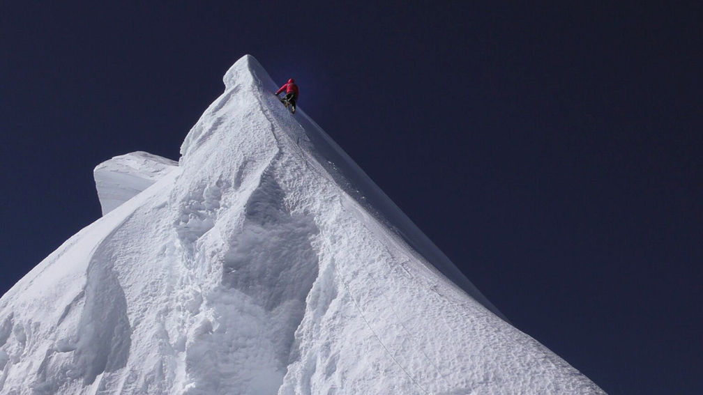 climber in red approach top of pyramidal snow peak