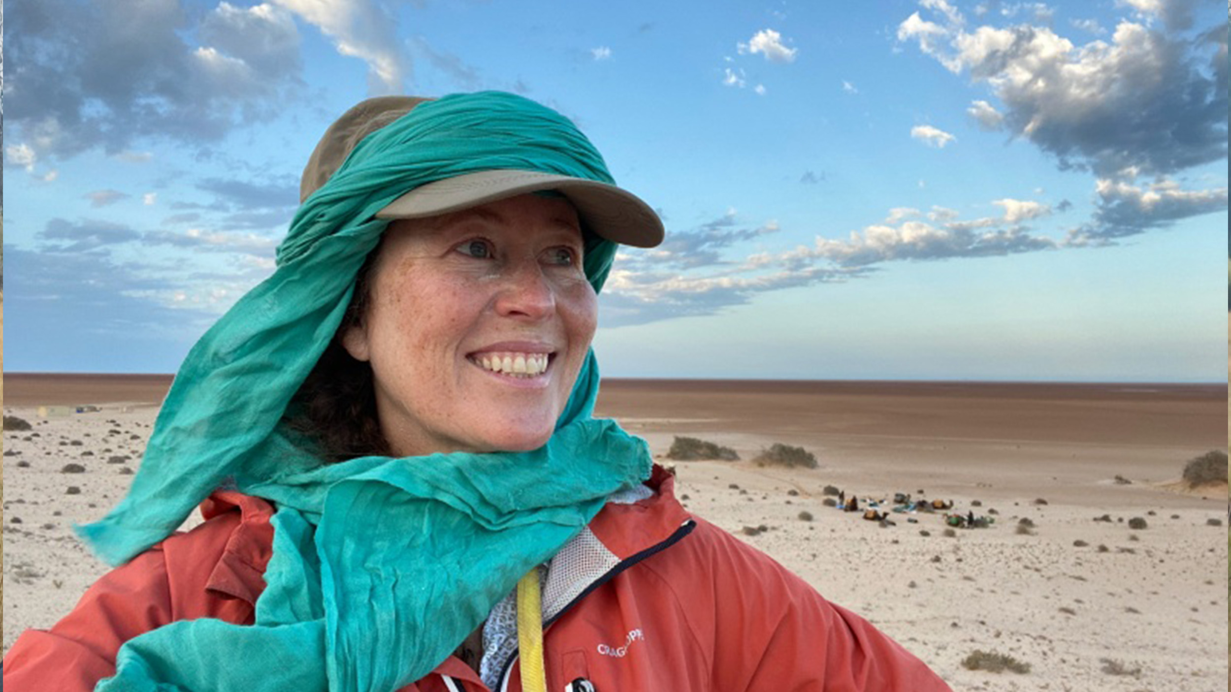 a woman smiles while standing in a desert