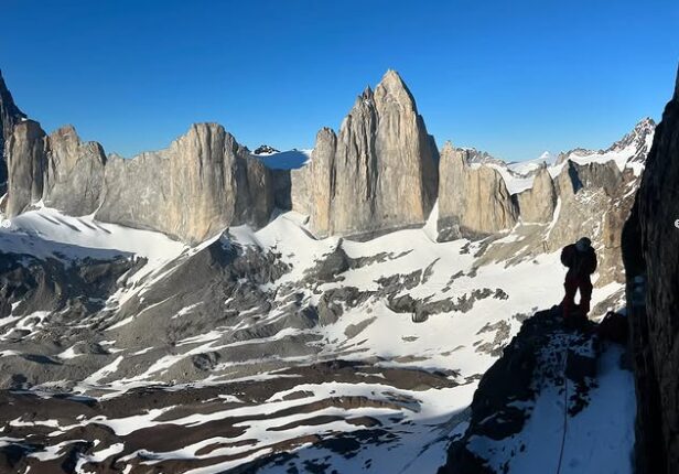 A climber on a ledge in the shade, Patagonian spires in background.