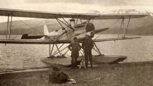 a photo of two men and a dog in front of a sea plane