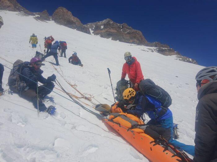 Rescuers help a sick climber in a stretcher on a snowy slope on Aconcagua