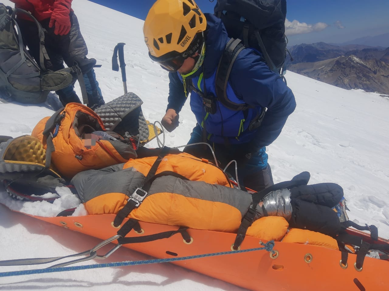 rescuers preapre to move a climber in a stretcher on a snowy slope.