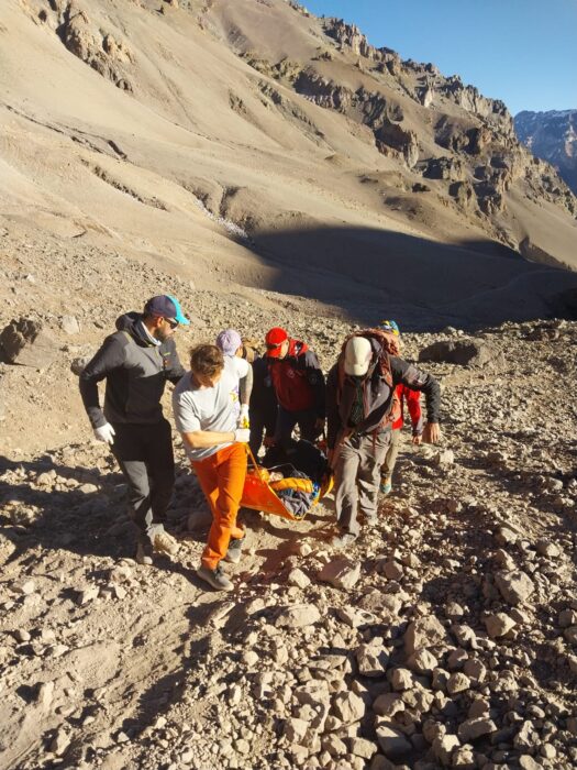 Several peopl carry astretcher on a scree slope