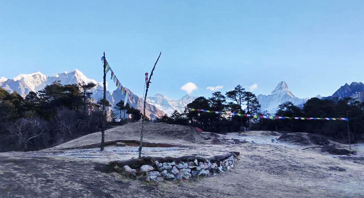 Two poles stand on an heli pad, one of them with a line of prayer flags.