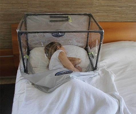 A woman sleeping with a bubble like tent covering her head and upper body. 