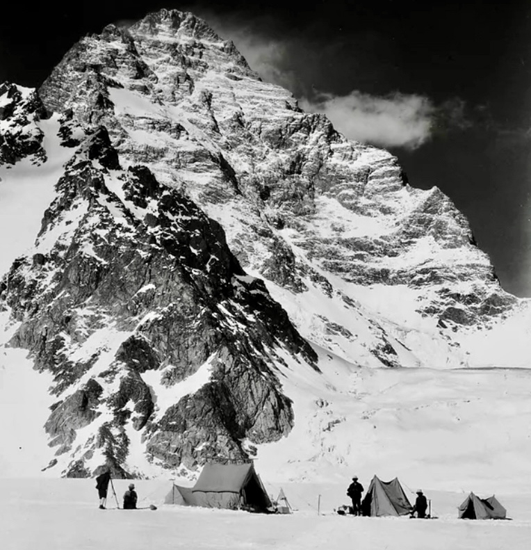 b/w archival photo of a camp in snow at the base of a giant peak