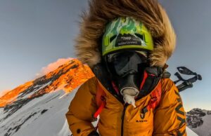 Jost Kobusch in full winter, high-altitude attire, with the summit of Everest shinning with alpenglow behind him.