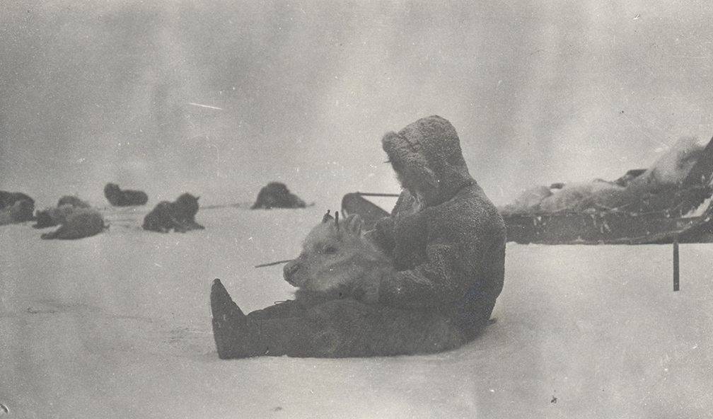 old b/w photo of Inuit man in furs sitting on the snow