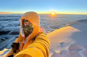 Lukas Furtenbach taakes a selfie on Everest as the sun rises behind him.