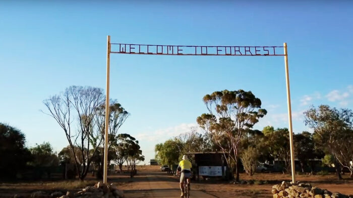 a man rides his bike under a wooden sign