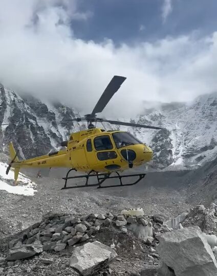 a yellow helicopter 2 meters above the rocky ground of a moraine.