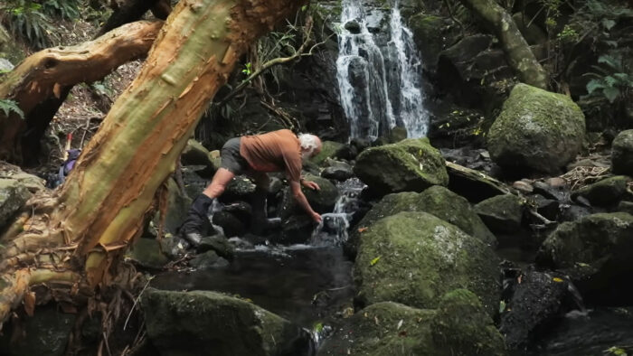 a man scoops a handful of water from a waterfall