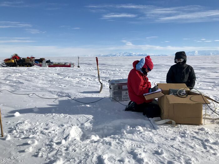 Two women next to unobtrusive electrical equipment in a snowy field.