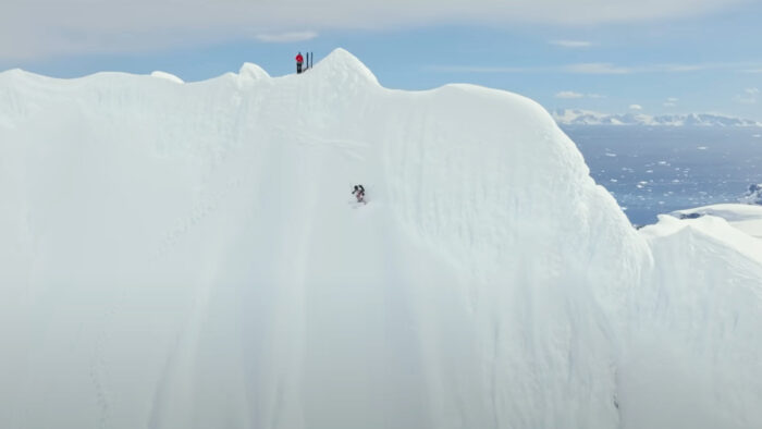 a wide shot of a woman descending a steep snow face on skis