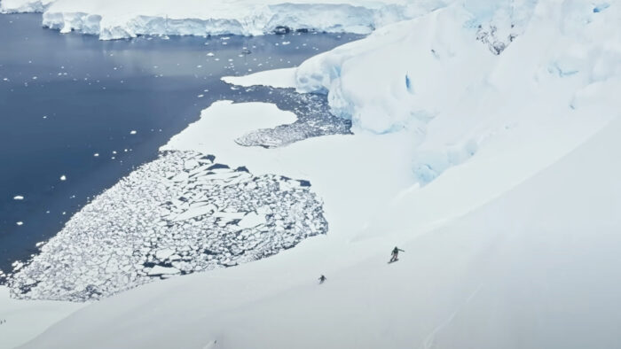 two people ski down a steep face