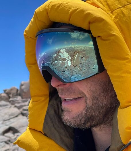 A climber with mirror-goggles that reflect a mainly rocky summit, Aconcagua