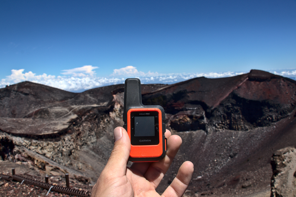 A hand holding an InReach, dark hills landscape near Mt Fuji