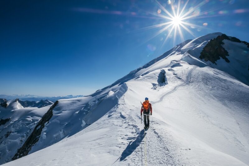 hiker on sunny day near top of snowy mountain