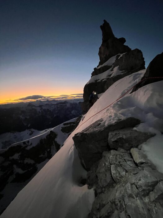 A climber with a headlamp approaches a rope to rappel down