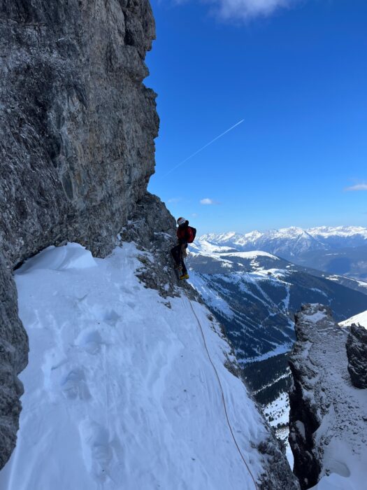 a climber on a traversing section of a face,between snow and rock