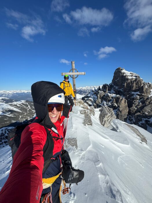 Climbers on a snowy summit with an iron cross on top.