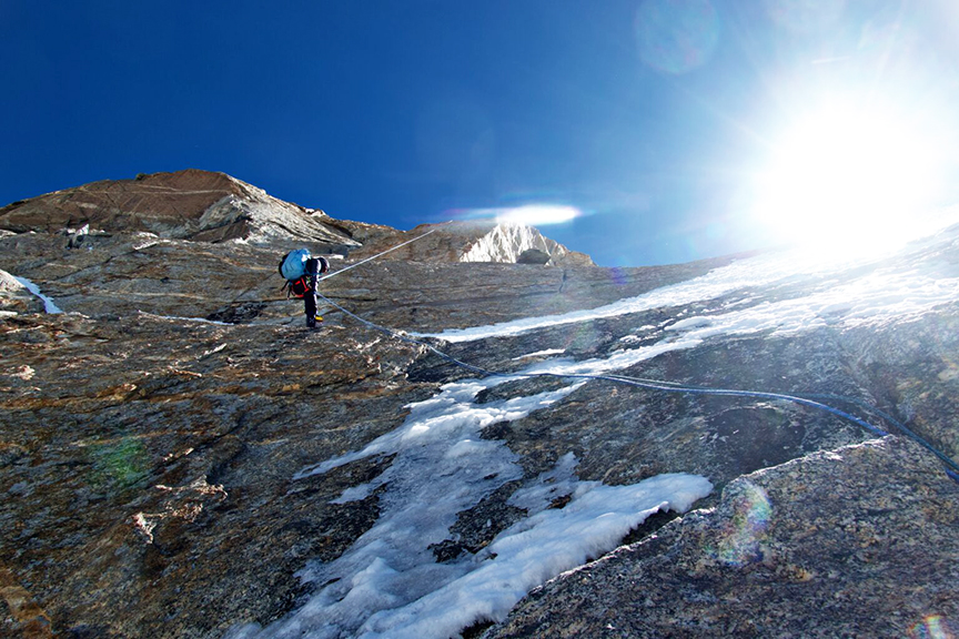 small climber on mixed face of rock and ice, backlit