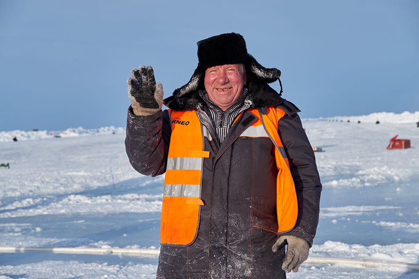 Russian man in orange vest waves in greeting in snowy landscape