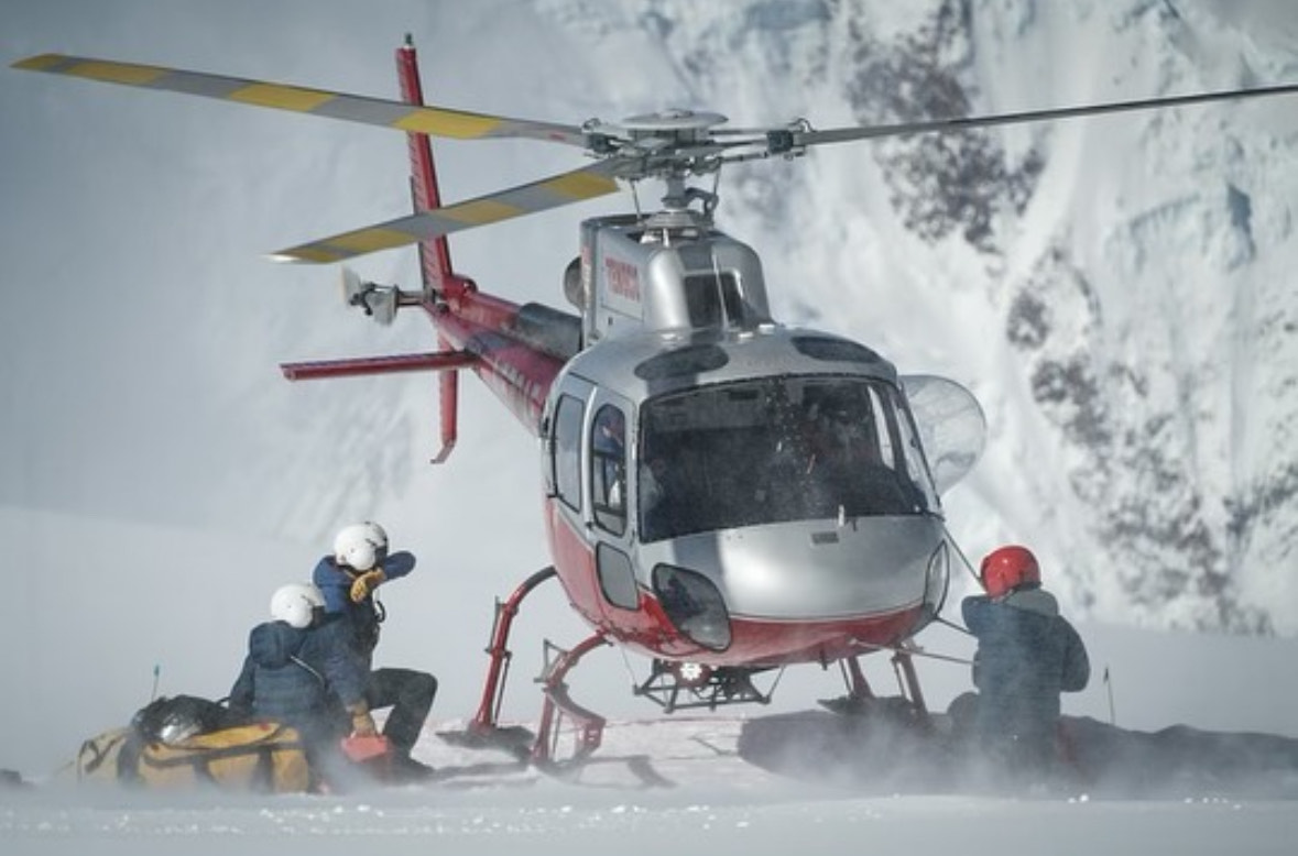 A helicoper poses n the snow while rescuers approach with a patient in a stretcher