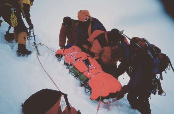 Several people help a climber in a stretcher on the snow