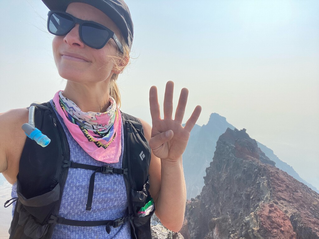 Close shot of Abbeg signaling "four" with her hand and dressed in trailrunning outfit.