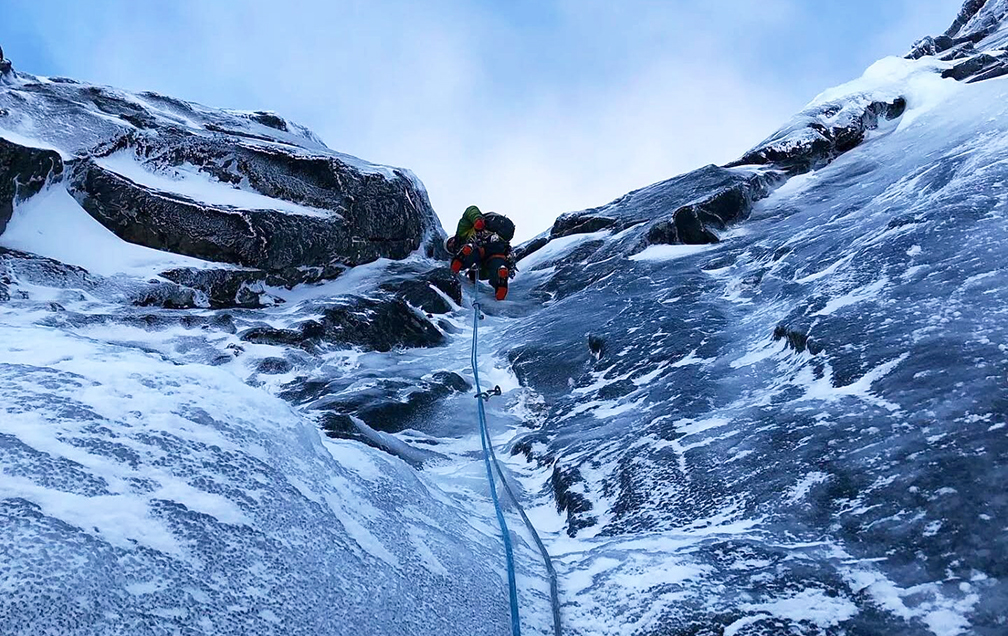 A climber at the top of a verglas-covered rock face