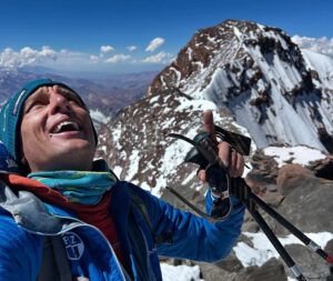 Egloff smiles and looks up on Aconcagua South summit, with the main summit on rock and snow behind.