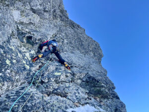 A climber with crampons on at a slightly overhanging rock face, with some patches of ice.