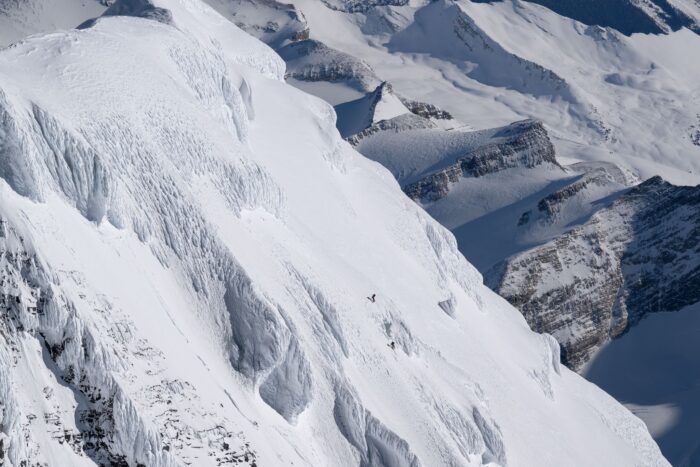 two tiny figures of skiers on a big, steep snow face, South face of Mt Robson