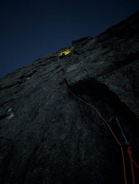 A granite face in the dark, with only the headlamp of a climber visible on the vertical rock. 