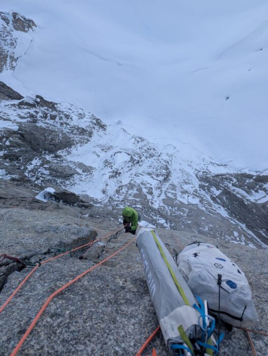 A climber on a granite wall in bad weather, as seen from a bivouac/belay