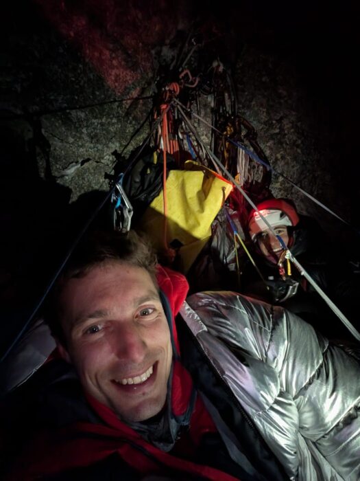 Two climbers smile to the camera during a bivy night on a portaledge.