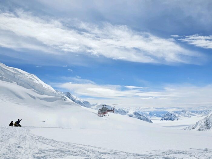 People wave thir arms to a helicopter while waiting on a snow field