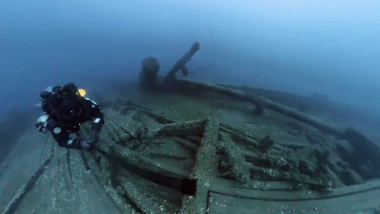 A diver underwater beside a shipwreck.