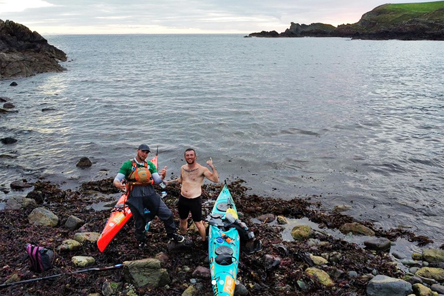 two kayakers pose on a rocky shore