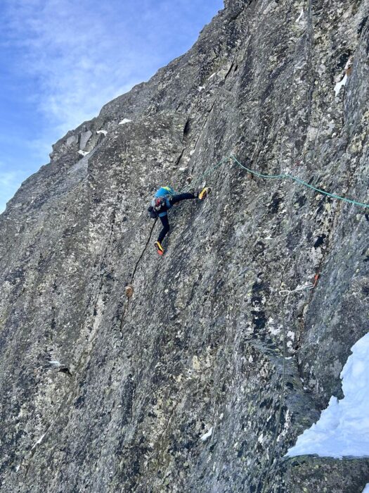 a climber with ice gear on a vertical, smooth rock section