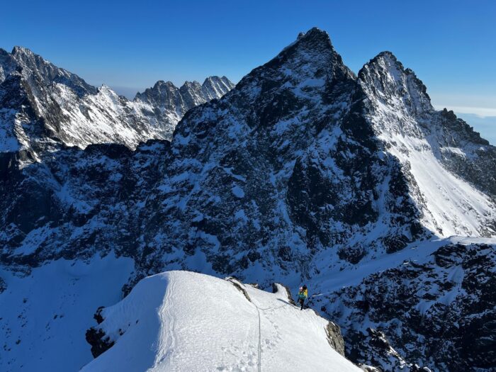 a climber on a snowy dome, on top of rocky-mixed ground. 