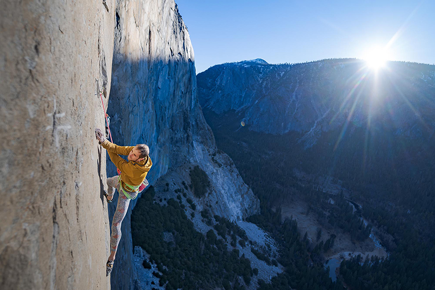 climber on a big wall with sun peeking above distant mountains