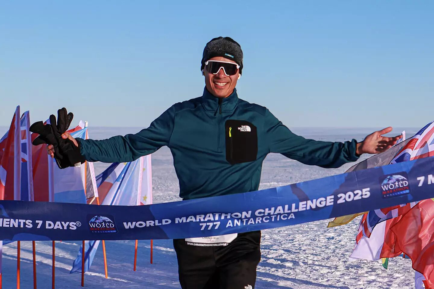 A man standing in front of a finish line, smiling.