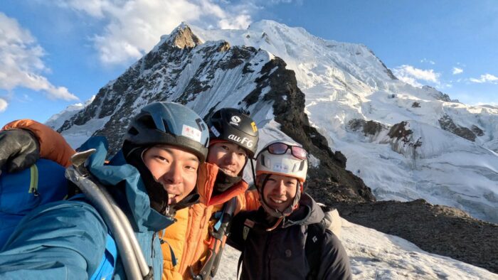 Three climbers smile on a mountain top. 